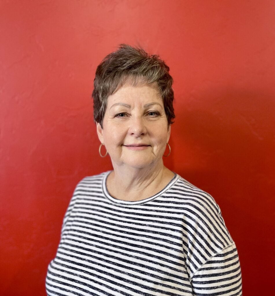 A woman in a striped shirt smiles in front of a red backdrop